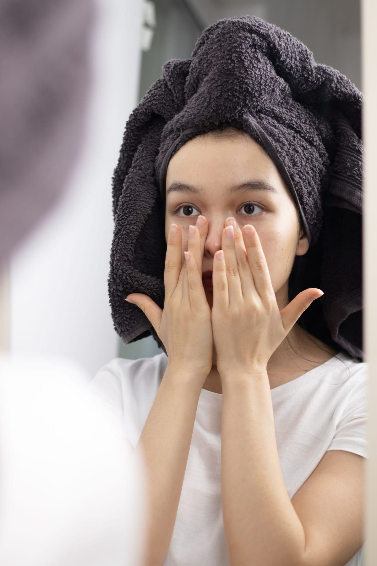 A woman with her hair wrapped in a towel pressing her hands gently to her face