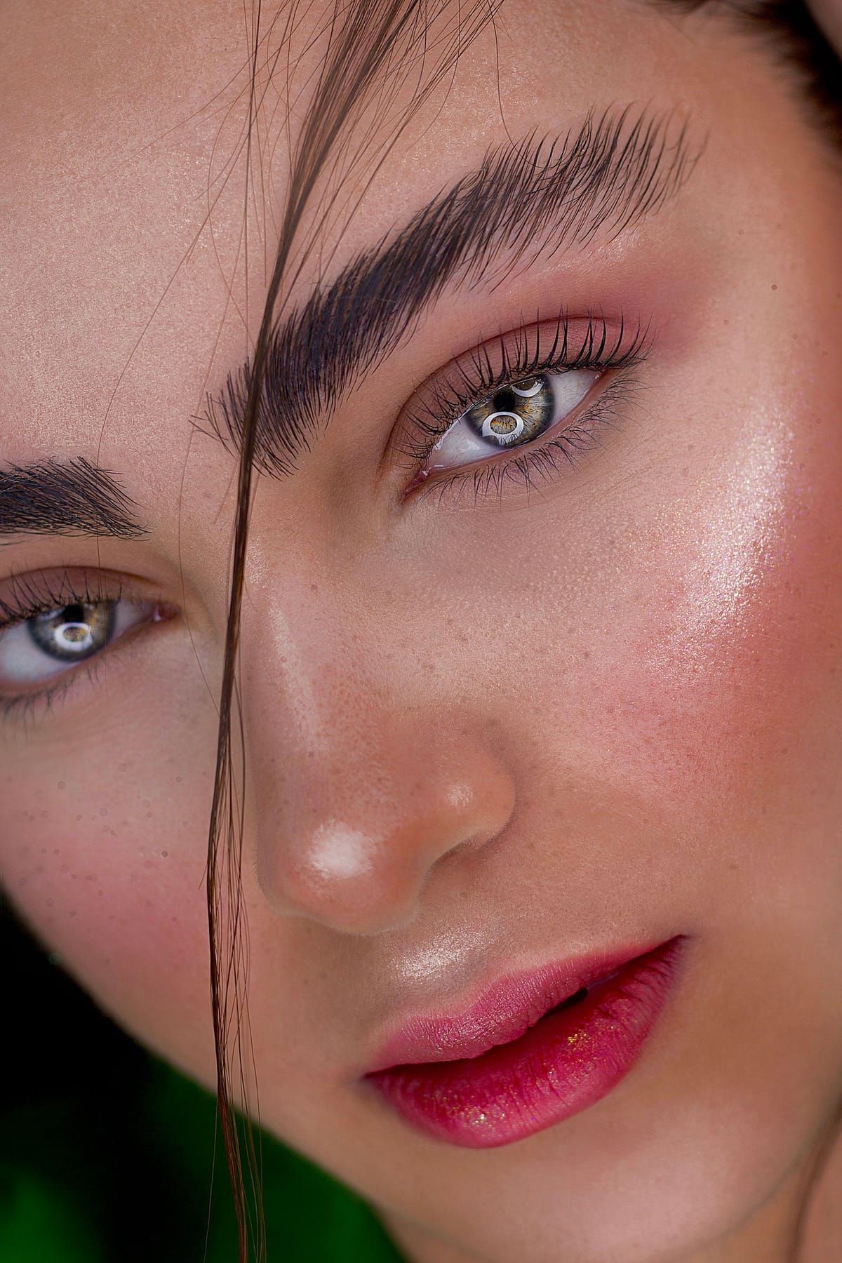 A woman with glowing skin, warm shimmery eyeshadow and a rosy lip smiling softly at the camera