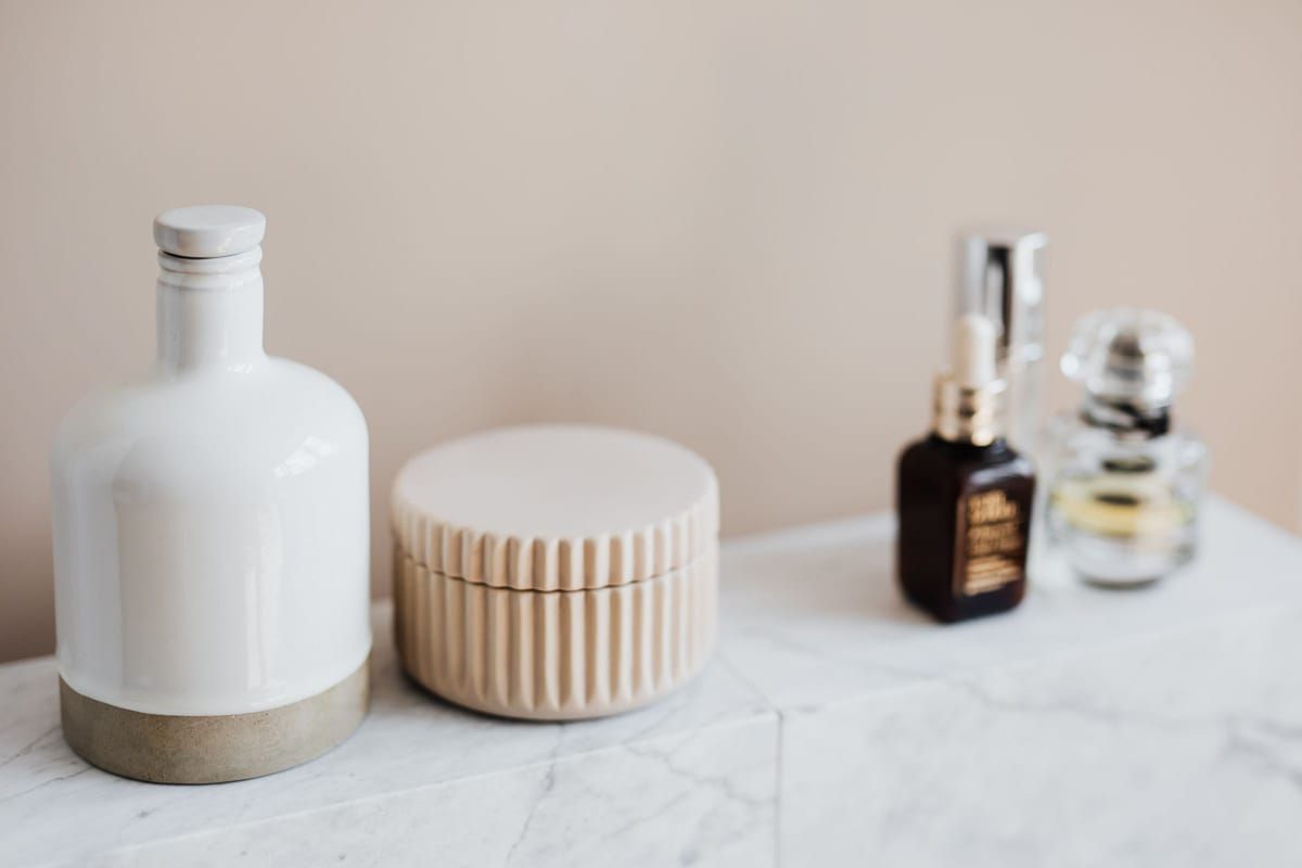 A marble bathroom shelf with a few skincare bottles, a serum and a ribbed jar of cream
