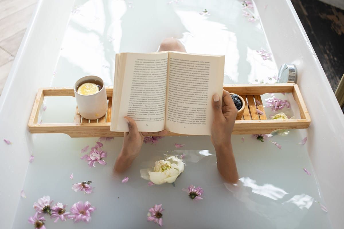 A bathtub with a wooden tray holding a candle, a book and a cup of tea
